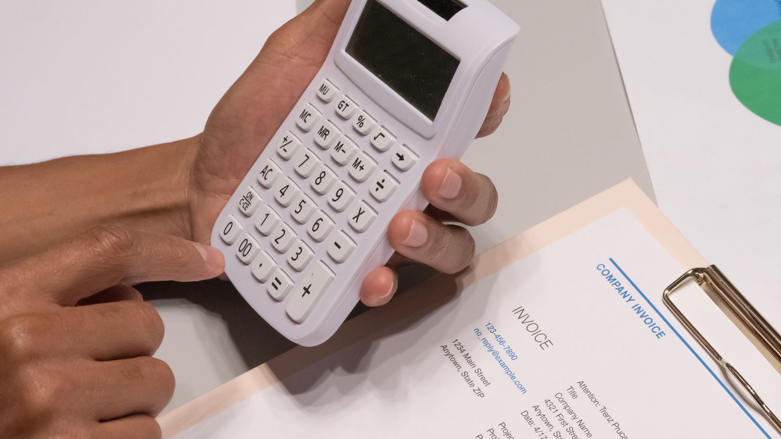 يد تكتب على آلة حاسبة بجانب أوراق فواتير وعرض سعر على مكتب خشبي