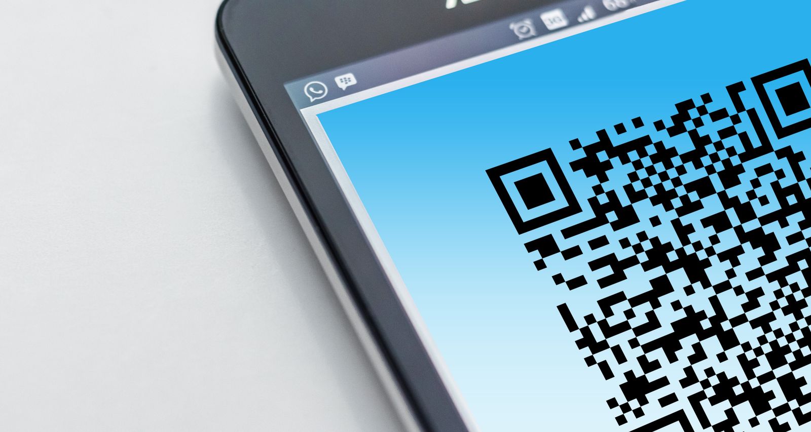 لقطة قريبة لشاشة هاتف ذكي تعرض رمز QR أسود كبيراً على خلفية زرقاء متدرجة، والهاتف موضوع على سطح أبيض.
