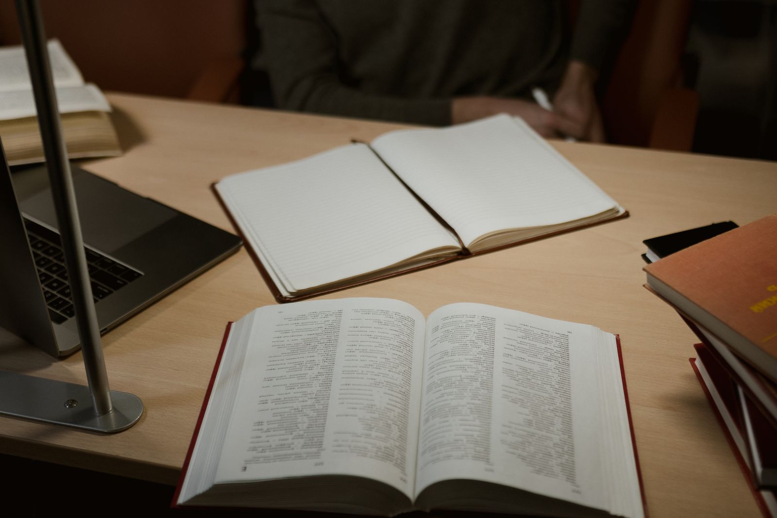دفتر ملاحظات فارغ إلى جانب كتاب مفتوح وحاسوب محمول على مكتب خشبي بإضاءة دافئة، استعداداً لتدوين الأفكار أثناء القراءة